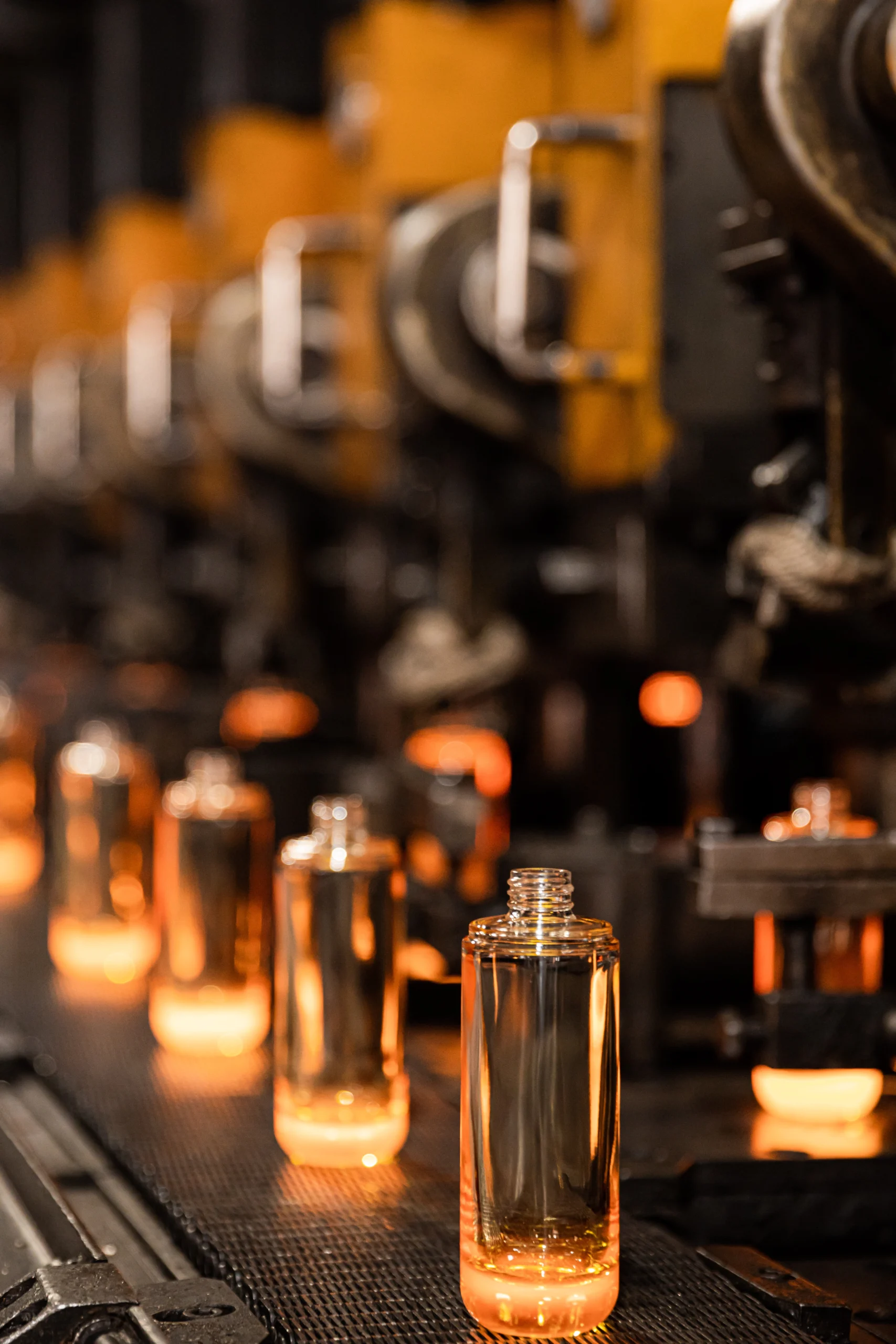 Amber glass cosmetic bottles on a production line under warm light, glass bottle manufacturing at the Jarsking factory